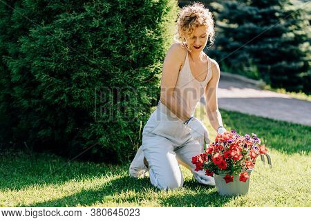 Blond Curly Happy Woman Gardener In White Gloves Sitting Near Plant Pot Holding Garden Spade With So