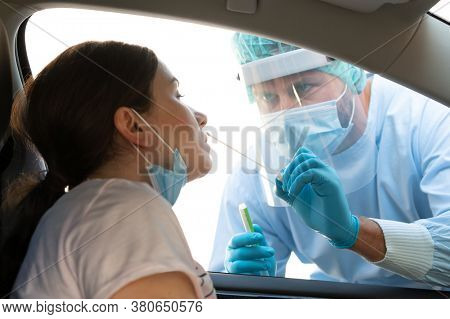 Woman getting tested at a coronavirus drive thru station by medical staff with PPE suit by throat swab. Health care drive thru service and medical concept