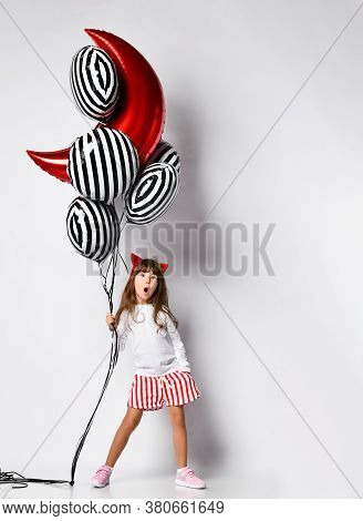 Girl In A White Sweater And Shorts, Hair Hoop With Red Horns Of Devil. She Holds A Bunch Of Balloons