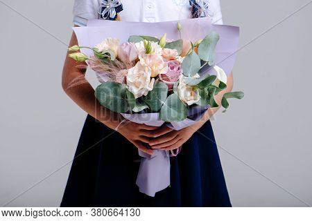 A Bouquet Of Flowers, Packed In Purple Paper In The Hands Of A Girl With Pigtails On A Light Backgro