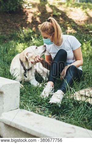 Front View Photo Of A Blonde Woman Wearing An Anti Virus Mask Lying On The Grass With Her Labrador