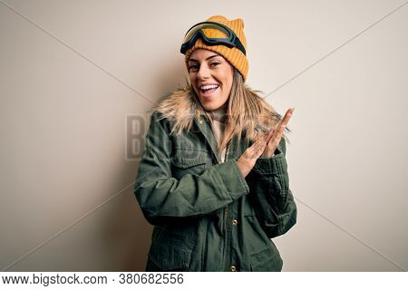 Young brunette skier woman wearing snow clothes and ski goggles over white background clapping and applauding happy and joyful, smiling proud hands together
