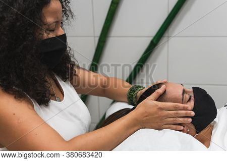 Latin Woman Applying Reiki On The Head Of A Young Woman During A Therapy, To Unlock The Crown Chakra