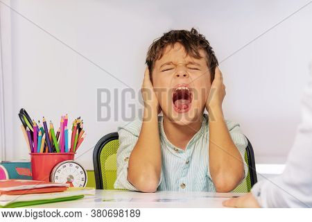 Autistic Boy Scream And Close Ears In Pain During Aba Development Therapy Sitting By The Table In Cl