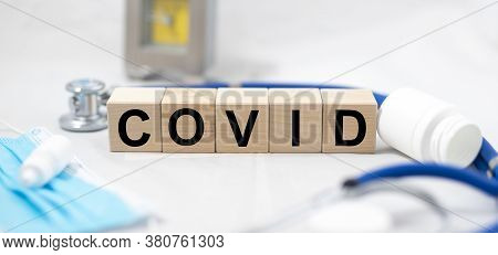 Covid Word On Cube Blocks On Light Table With Jar Of Pills Stethscope And Mask On White Background