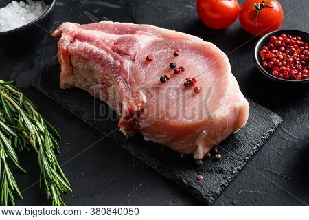Raw Pork Chop Steak And Salt, Pepper On Black Slate Stone Board With Rosemary, And Fresh Ingredients
