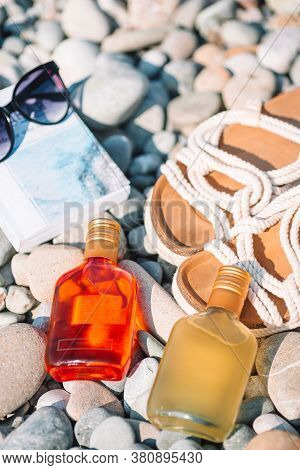 Beach Hat On Opened Book With Sunscreen And Shoes On Pebble Beach