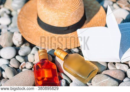 Beach Hat On Opened Book With Sunscreen And Shoes On Pebble Beach