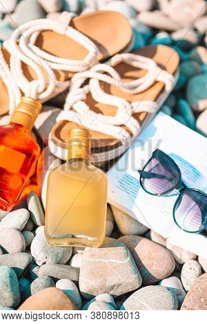Beach Hat On Opened Book With Sunscreen And Shoes On Pebble Beach