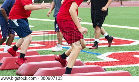 High School Football Players At Summer Camp Running Sideways Over Red Barriers While The Coaches Wat