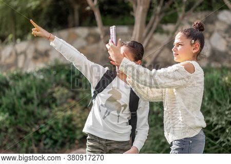 Two Teenager Girls Take A Photo With Smartphone Outdoor. Young Teen Girls, Small Groups Travelers Ta