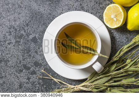 White Cup Of Herbal Sage Tea With Dried Sage Leaves And Lemon On Grey Rustic Background. Herbal Tea 