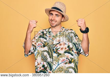 Young handsome man with blue eyes on vacation wearing summer florar shirt and hat celebrating surprised and amazed for success with arms raised and open eyes. Winner concept.