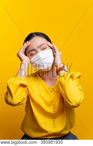 Asian Woman Wearing Protective Face Mask Was Sick With Headache And Touch Her Head Isolated On Yello