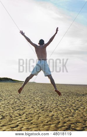 Widok z tyłu przystojny młody człowiek robi gwiazda skok na plaży