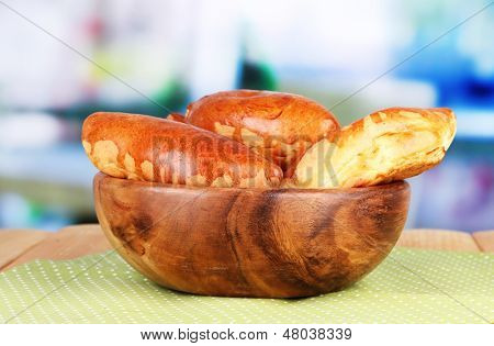 Empanadillas al horno frescos, en un recipiente de madera, en la mesa de madera, sobre fondo brillante