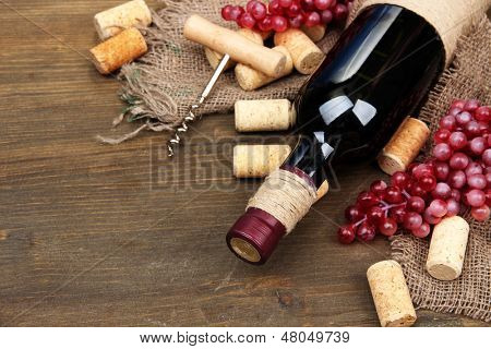Botella de vino, uvas y corchos sobre fondo de madera