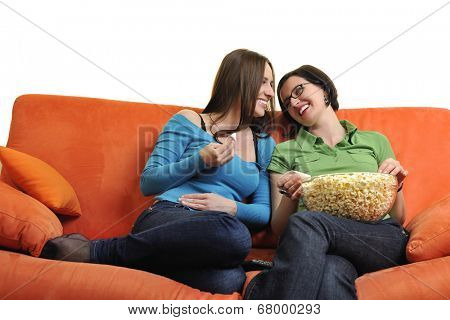 female friends eating popcorn and watching tv at home on orange sofa isolated on white