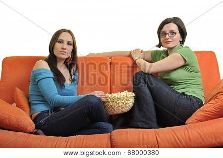 female friends eating popcorn and watching tv at home on orange sofa isolated on white