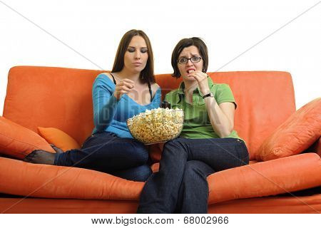 female friends eating popcorn and watching tv at home on orange sofa isolated on white