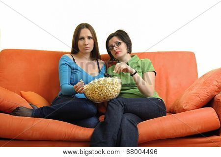 female friends eating popcorn and watching tv at home on orange sofa isolated on white