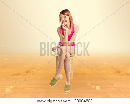 Redhead Girl Sitting On Wooden Chair Over Ocher Background