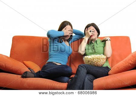 female friends eating popcorn and watching tv at home on orange sofa isolated on white