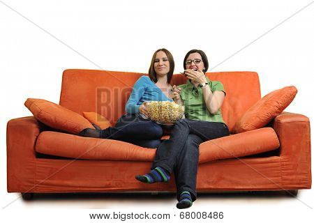 female friends eating popcorn and watching tv at home on orange sofa isolated on white
