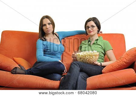 female friends eating popcorn and watching tv at home on orange sofa isolated on white