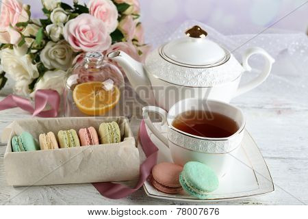 Colorful macaroons with cup of tea on color wooden table, on light background