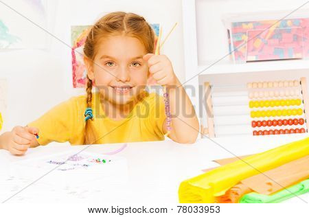Little beautiful blond girl puts beads on string