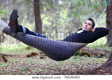 Handsome Young Man Lies In Hammock In Woods At Dull Autumn Day