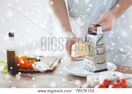 cooking, food, people and home concept - close up of male hands with grater, vegetables and olive oil grating cheese in kitchen