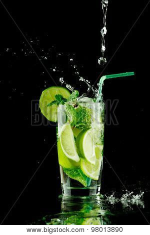 Pouring fresh mojito cocktail in glass isolated on black background