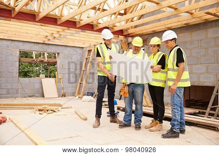 Builder On Building Site Looking At Plans With Apprentices