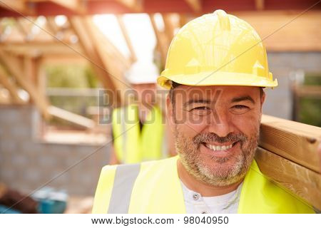 Builder And Apprentice Carrying Wood On Construction Site
