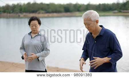 Asian Senior Elderly Couple Practice Taichi, Qi Gong Exercise Next To The Lake