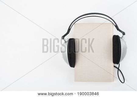 Audiobook on white background. Headphones put book, empty cover, copy space for ad text. Distance education, e-learning concept