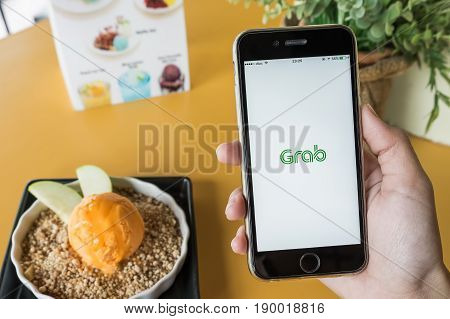 CHIANG MAITHAILAND - JAN 72017 : A MAN hand holding Grab app showing on iphone 6s with cheese ice Cream on Yellow table. Grab is smartphone app-based transportation network