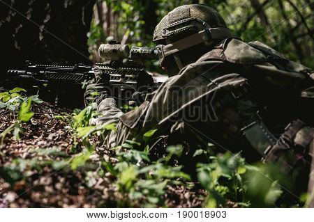 Soldier with submachine gun lies in ambush at forest