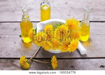 Fresh yellow flowers tussilago in mortar on wooden background. Wellness setting. Selective focus.