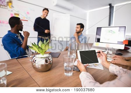 Cropped image of businesswoman using digital tablet while colleagues discussing in meeting room at creative office