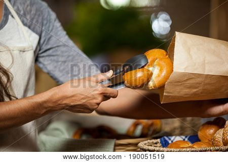Mid-section of staff packing bread in paper bag at bakery shop