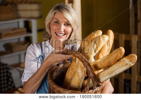 Female staff holding basket of baguettes in bakery section of supermarket