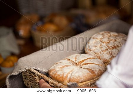 Hand of female staff holding basket of sweet foods in bakery section of supermarket