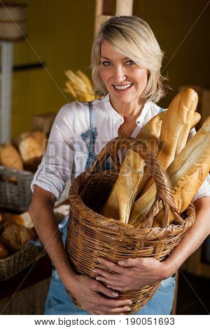 Female staff holding basket of baguettes in bakery section of supermarket