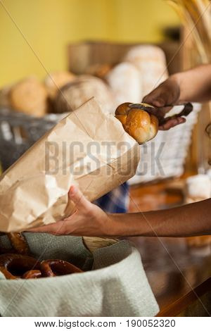 Mid-section of staff packing bread in paper bag at bakery shop