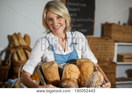 Female staff holding basket of bread in bakery section of supermarket