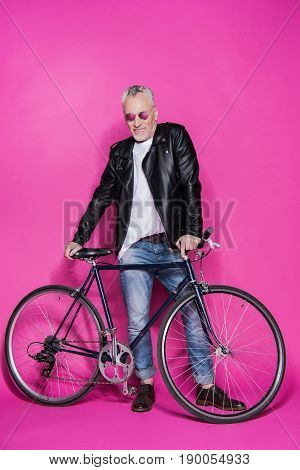 Smiling Fashionable Senior Man Wearing Leather Jacket And Sunglesses Standing With Bicycle Isolated