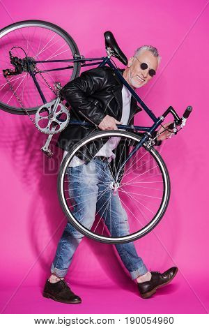Stylish Senior Man Wearing Leather Jacket And Sunglesses Holding Bicycle On His Shoulders Isolated O